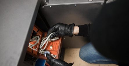 Hands opening a home safe containing a watch and a pearl necklace inside a lined jewelry drawer